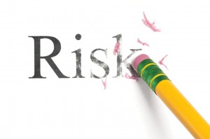 The word, Risk, being erased by a yellow pencil with a green band and eraser crumbs scattered about.