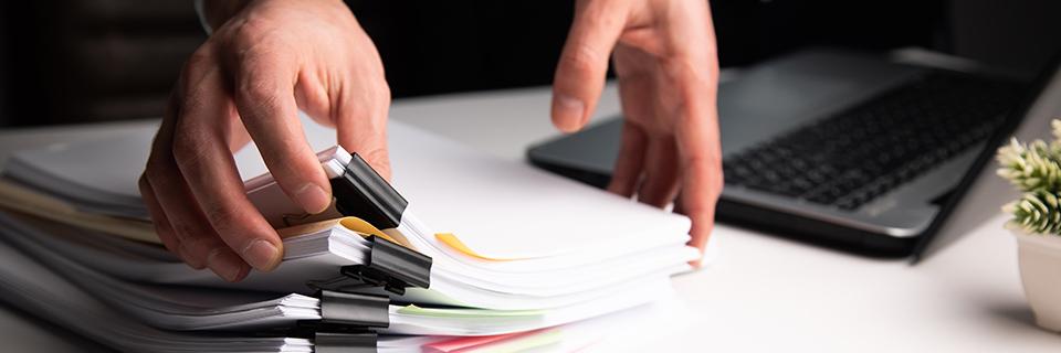 A person holding a stack of documents on a desk.