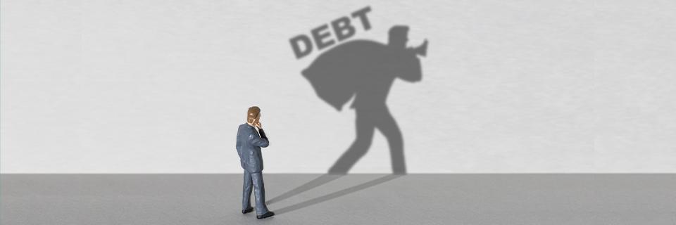 A figurine looking at his own shadow, carrying a bag of loaned funds over his shoulder, and the word debt above.