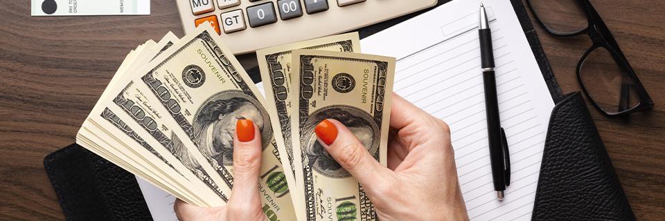 A person holding money in their hands with a calculator and a notebook on a desk.