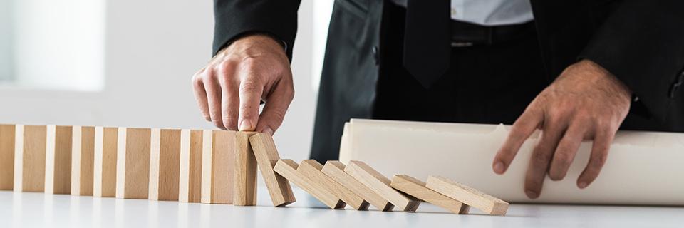 A hand stopping a domino effect, symbolizing the United States Citizenship and Immigration Services investment sustainment period.