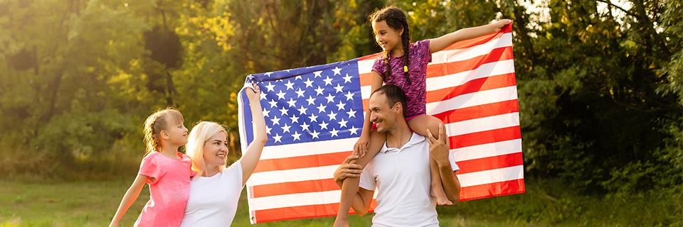 A family of foreign nationals smiling and holding up the American flag.