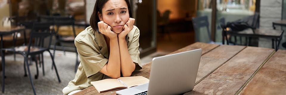 A person sitting at a table in front of a computer with her hands on her face, looking distressed over her green card application.