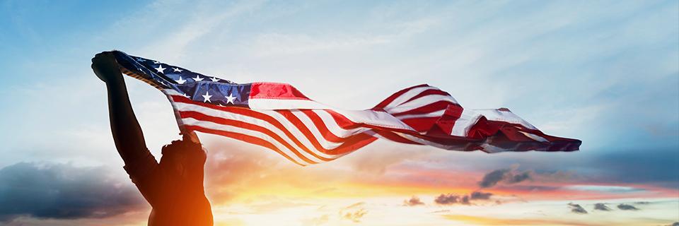 An EB-5 investor standing outdoors in sunset, holding up an American flag.