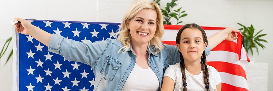 A family of non immigrant visa holders who applied to change their legal status to lawful permanent resident status smiling at the camera and holding up the American flag.