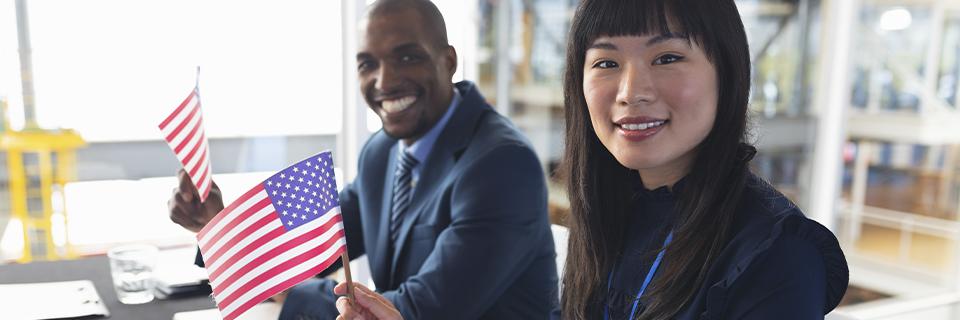 An EB-5 expert and an investor smiling at the camera and holding American flags.