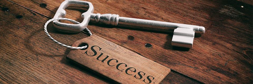 A key on a wood surface, with the word success written on the keychain.