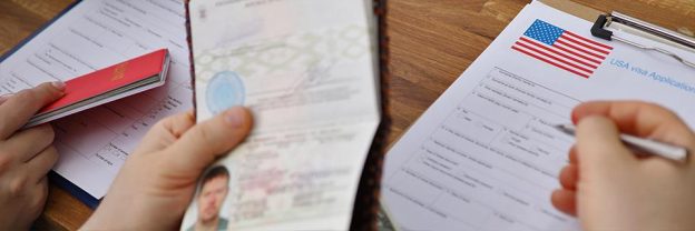 A hand filling out a U.S. visa application document.