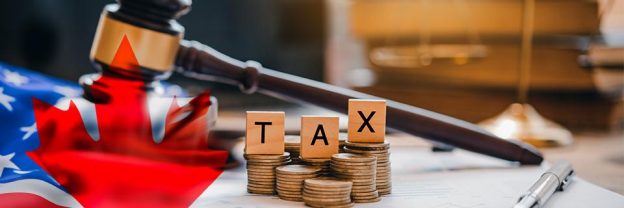 A stack of coins with the letters TAX on them. There is a Canadian flag and American flag on the corner, with a judge's gavel in the back.
