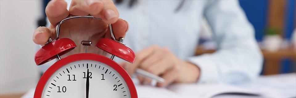 A hand holding a red alarm clock.