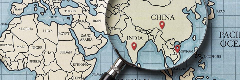 A magnifying glass on a world map with pins on China, India and Vietnam.