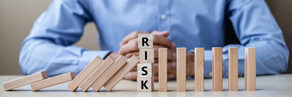 Wooden blocks with risk written on them stopping a domino effect.
