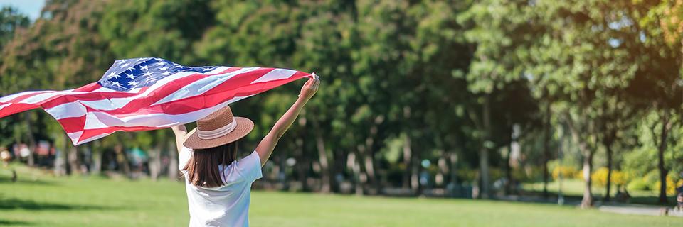 A person holding up an American flag outdoors, celebrating the success of her visa status application process.
