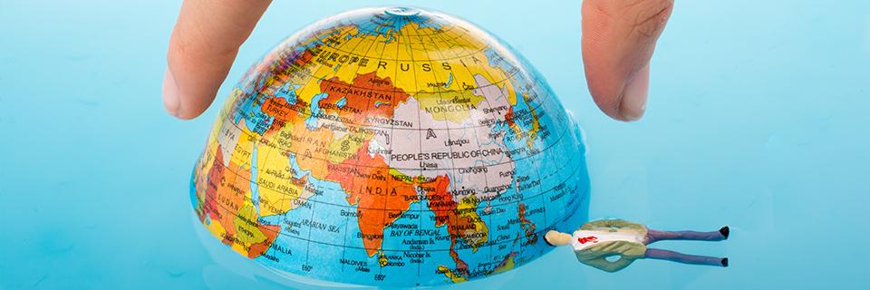 A hand holding half a globe, with a figurine below it.
