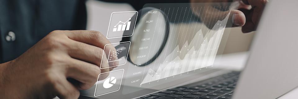 A person using a magnifying glass to look at graphs on a computer screen.