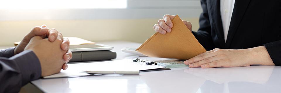 A person sitting opposite a government official, holding supporting documents in their hand in an envelope.