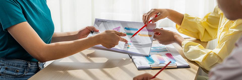 A group of people holding pens and pointing at some graphics or financial documents.