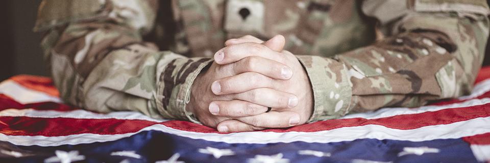 A close-up of a soldier's hands folded on a U.S. flag.