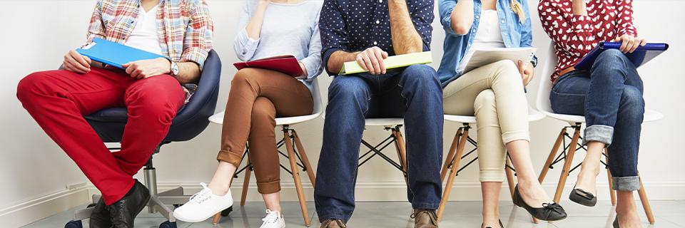 A group of people sitting in chairs with application documents and folders in their hands.