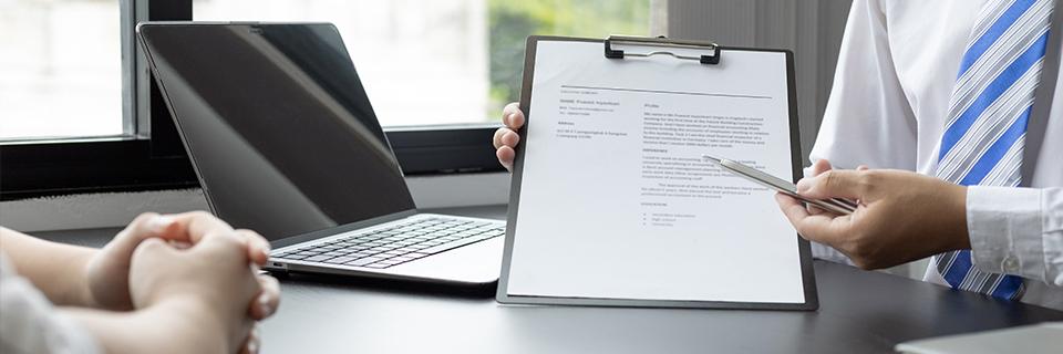 A hand holding a clipboard, showing some documents to an interviewee.