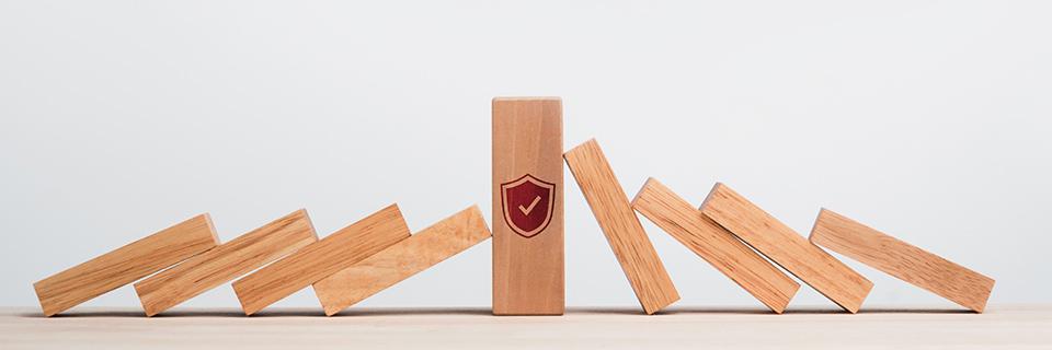 A block of wood with a shield icon on it, next to other wooden blocks representing a domino effect.