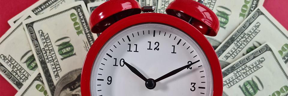 A red alarm clock in front of a stack of dollars, symbolizing priority processing for rural eb5 investments.