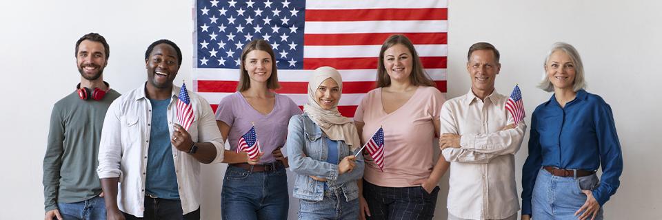 A group of EB5 investors standing in front of an American flag and smiling at the camera.