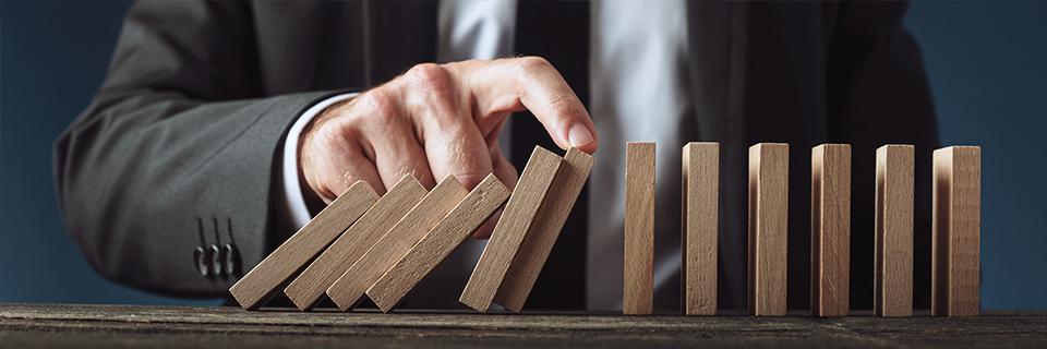 A hand stopping a domino effect with wooden block, symbolizing low-risk eb5 project selection.