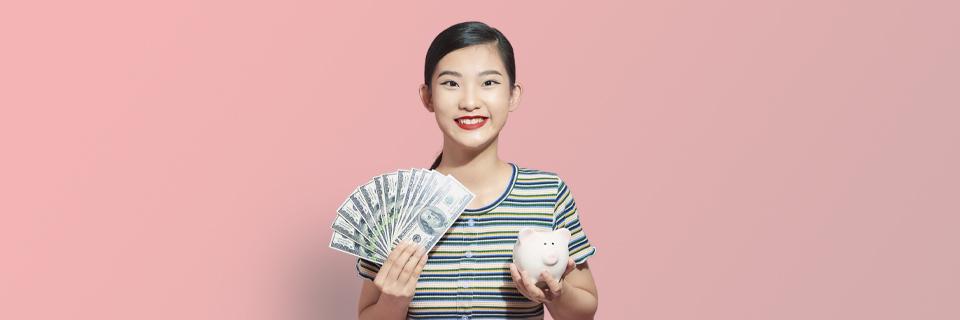 An Asian EB5 investor holding some money in one hand and a piggy bank in the other.