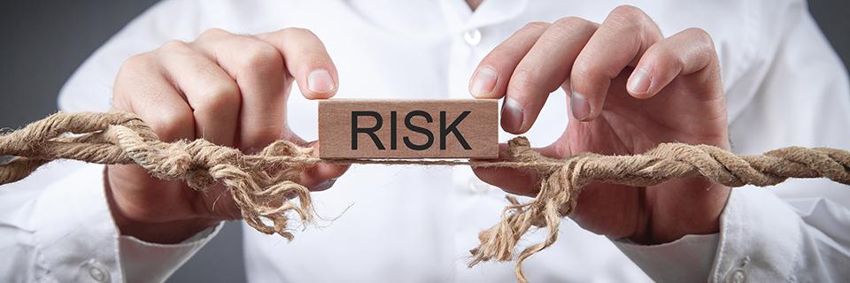 A person holding a wooden block that spells out risk on top of a breaking rope, symbolizing the benefits of EB5 repayment guarantees.
