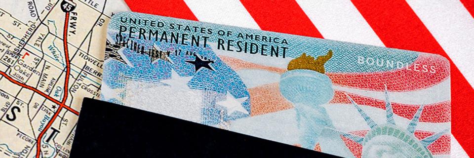 A close up of a green card inside a passport, with the American flag behind it.