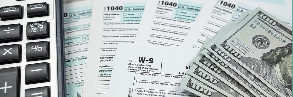 A close-up of a stack of dollars, some tax return documents and a calculator, symbolizing EB5 source of funds.