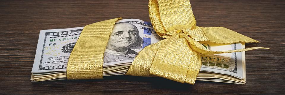 A stack of U.S. dollars tied with a gift wrap.