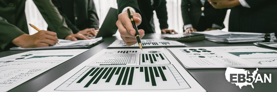 A group of EB5 industry professionals going over some investment data, with the EB5AN logo on the corner.