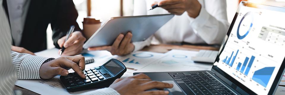 A group of regional center professionals working at a desk using tablets, computers and calculators.