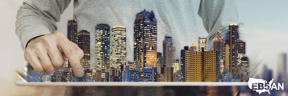 A conceptual image showing a hand manipulating a city skyline on a tablet, symbolizing the future of EB5 investments and the importance of Guaranteed Maximum Price (GMP) contracts in real estate development.