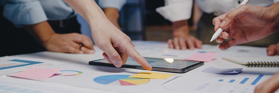 Hands pointing at financial charts and graphs on a tablet during a team meeting, representing EB5 project monitoring and data-driven decision-making.