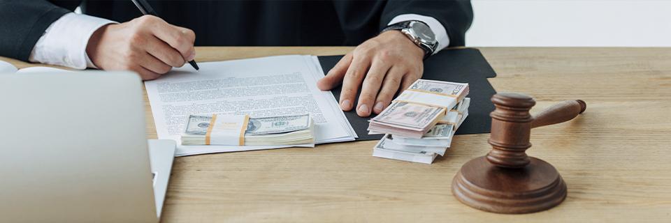 An immigration attorney signing documents with stacks of money and a gavel on the table. The EB5 Immigrant Investor Program allows foreign nationals to gain U.S. Green Cards through lawful investments in job-creating projects.