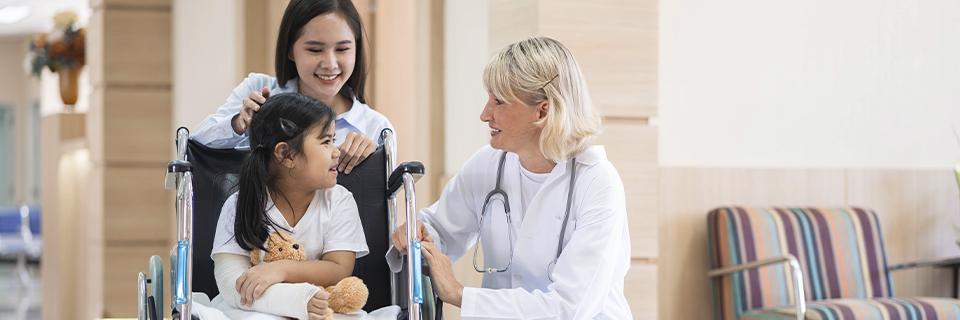 Female doctor interacting with a child in a wheelchair alongside a caring mother, symbolizing the family-friendly healthcare advantages available to EB5 Green Card holders in the U.S.