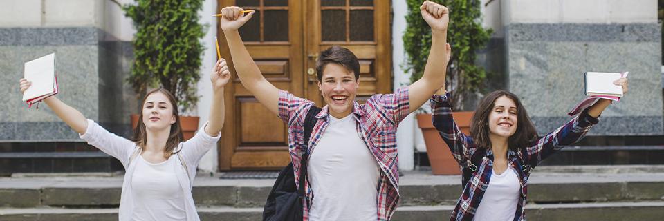 Three students joyfully celebrating outside a building, representing the educational opportunities available through an EB5 Green Card, including domestic tuition rates and expanded access to American universities.