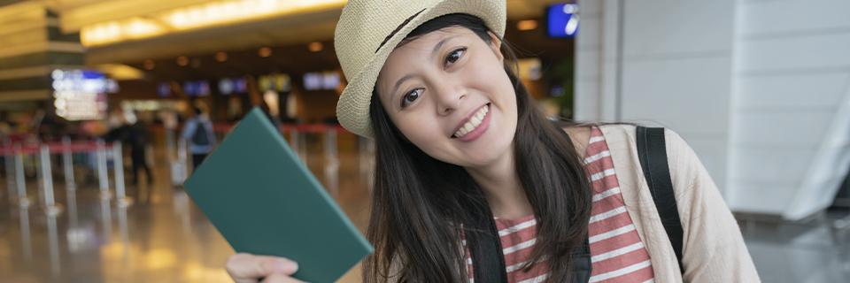 A smiling traveler holding a passport at an airport, showcasing the convenience and stability of permanent residency through the EB5 Green Card for international students pursuing education in the US.