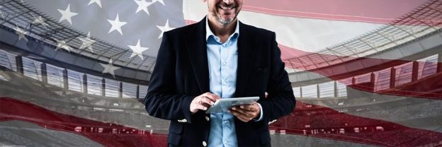 Confident businessman holding a tablet with the U.S. flag in the background, symbolizing the American Dream through EB5 investment opportunities.