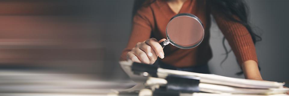 Woman closely examining documents with a magnifying glass, highlighting the importance of investigating EB5 company reputation and track record.