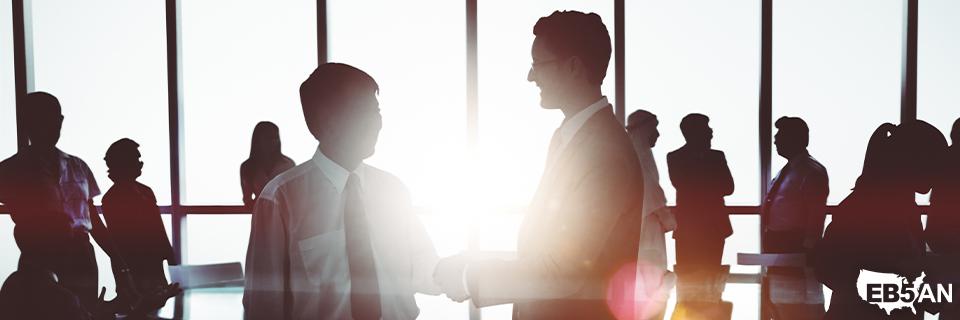 The EB5AN logo next to business professionals shaking hands in a corporate setting, symbolizing trust and collaboration in EB-5 investment leadership.