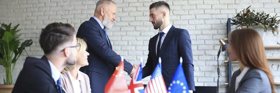 wo business professionals shaking hands during a meeting with international flags in the background, highlighting the global scope of the E2 Treaty Investor Visa.