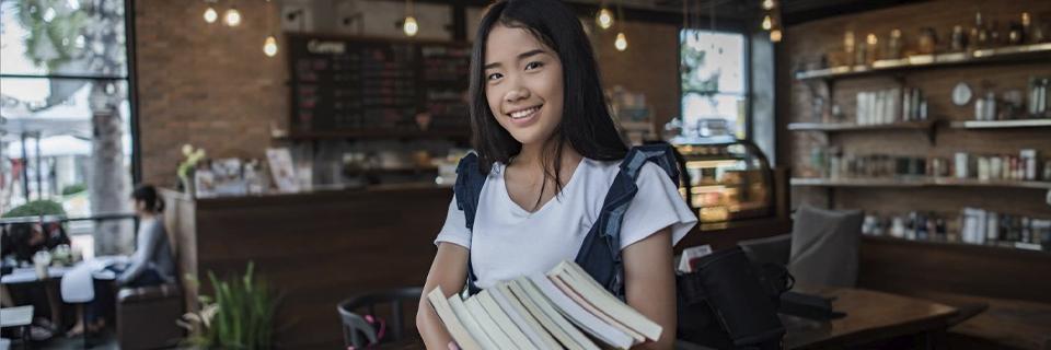 Happy student holding books in a cozy café setting, representing the enhanced educational opportunities available to EB5 Green Card holders in America.