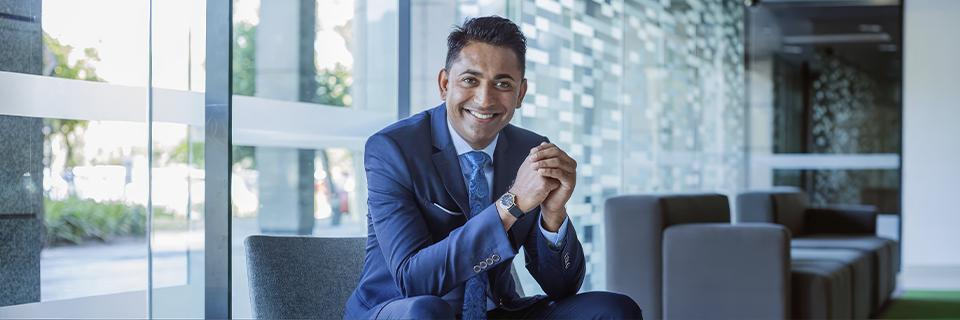 Smiling EB5 investor in a suit sitting in a modern office, symbolizing the opportunities offered by the EB5 Immigrant Investor Visa for securing a green card in America.