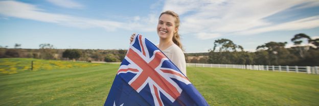 Smiling Australian woman holding up a flag, symbolizing how Australians can apply for a U.S. Green Card through employment-based, family-sponsored, and EB5 investor visa programs.