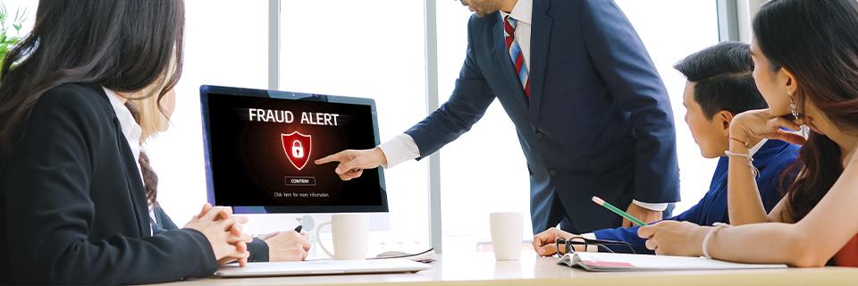 Regional center team in a conference room looking at a computer screen displaying a “Fraud Alert” message, emphasizing the importance of avoiding EB5 fraud risks.