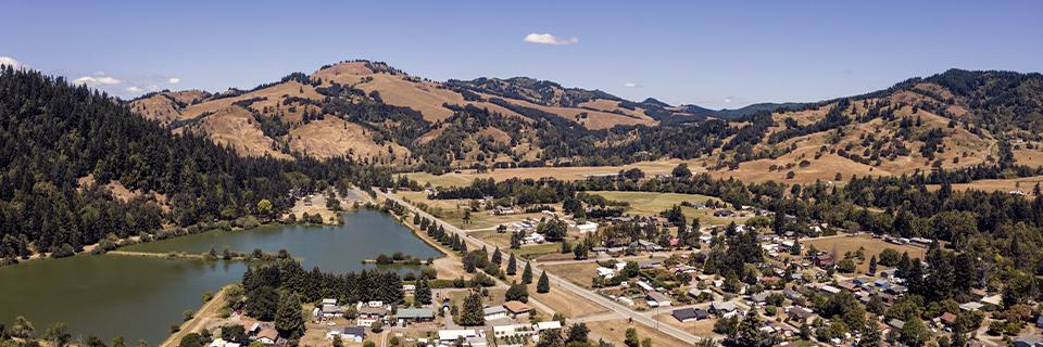 Aerial view of a small town surrounded by rolling hills and a lake, representing rural TEA locations in the EB5 program. Rural EB5 projects offer reserved visas and faster processing for investors.